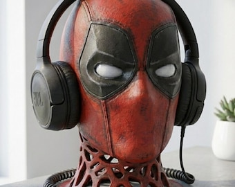 May include: A red and black Deadpool head bust with black headphones. The bust has a detailed design, with a textured appearance. The headphones are black and have the JBL logo. The bust is on a decorative base.