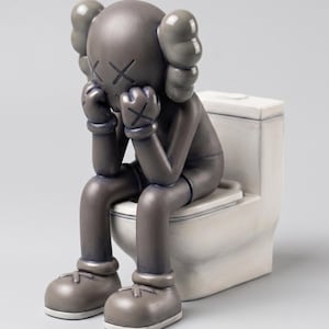 May include: A grey vinyl collectible figure with X-shaped eyes and bone-like ears, sitting on a white toilet. The figure has its hands raised to its head in a pensive pose, featuring smooth, matte-finished surfaces and rounded, cartoonish limbs.