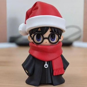 Op de afbeelding: Een beeldje van een personage met een rode kerstmuts met een witte rand, een zwarte bril, een rode sjaal en een zwarte jas. Het beeldje heeft zwart haar en is een feestelijke vakantiedecoratie.