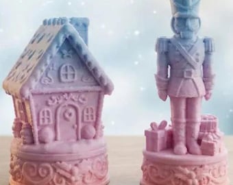 Könnte beinhalten: Weihnachtsdekorations-Set. Ein rosa-blaues Lebkuchenhaus und eine Nussknacker-Soldatenfigur. Das Haus hat ein detailliertes Dach und Fenster. Der Soldat steht auf einem Sockel mit Geschenken. Festliche Weihnachtsdekoration.