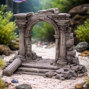 May include: A detailed aquarium decoration featuring a miniature, weathered stone archway with two columns and a broken pillar. The gray structure is set on a sandy base, with a small fish swimming above. The background includes green plants and rocks.