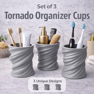 May include: Set of three gray tornado organizer cups. Each cup has a unique design and holds bathroom essentials like toothbrushes, toothpaste, a soap dispenser, comb, and brush. The text on the image reads "Set of 3 Tornado Organizer Cups" and "3 Unique Designs."