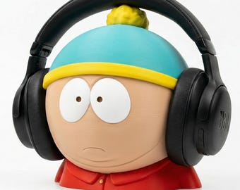 May include: A figurine of a cartoon character wearing black JBL headphones. The character has a light blue hat with a yellow brim, a red jacket, and a neutral skin tone. The headphones are over-ear style.