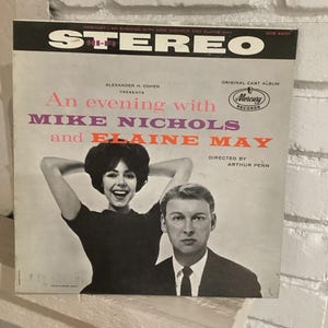 May include: Vintage vinyl record album cover for "An Evening with Mike Nichols and Elaine May." The cover features a black and white photo of the two performers. The album title is in pink and orange text.