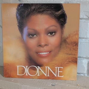 Puede incluir: Portada del álbum con un primer plano de Dionne Warwick. La portada tiene una paleta de colores cálidos con un retrato de la cantante con una prenda de piel. La palabra "DIONNE" está impresa en letras blancas grandes.