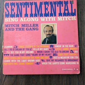 Pode incluir: Capa de álbum de vinil vintage para "Sentimental Sing Along With Mitch" de Mitch Miller and The Gang. A capa é rosa com texto azul e um retrato de Mitch Miller. Os títulos das músicas estão listados abaixo.