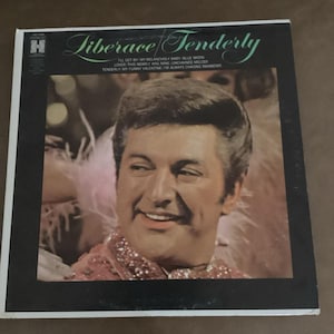 May include: Vintage vinyl record album titled "Liberace Tenderly." The album cover features a portrait of Liberace smiling. The album's tracklist includes "I'll Get By," "My Melancholy Baby," and "Blue Moon." The album is in a black frame.