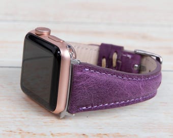 May include: A rose gold Apple Watch with a purple leather band. The band has a textured finish and is stitched with white thread.