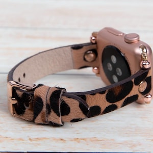 May include: A rose gold Apple Watch with a leopard print leather band. The band has gold studs and a rose gold buckle.