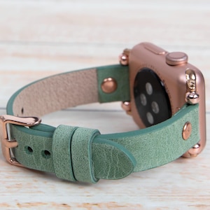Pode incluir: Uma pulseira de relógio de couro verde com ferragens de ouro rosa e um Apple Watch de ouro rosa.