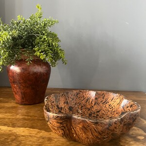 K&ouml;nnte beinhalten: Eine braune Holzschale mit einem welligen, unregelm&auml;&szlig;igen Rand und einem dunkelbraunen und schwarzen Marmormuster.