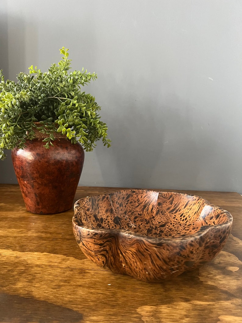 K&ouml;nnte beinhalten: Eine braune Holzschale mit einem welligen, unregelm&auml;&szlig;igen Rand und einem dunkelbraunen und schwarzen Marmormuster.