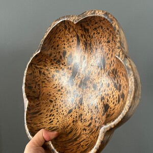 K&ouml;nnte beinhalten: Eine braune Holzschale mit einem einzigartigen Marmormuster. Die Schale hat eine blumenartige Form mit f&uuml;nf abgerundeten Lappen.