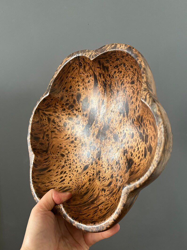 K&ouml;nnte beinhalten: Eine braune Holzschale mit einem einzigartigen Marmormuster. Die Schale hat eine blumenartige Form mit f&uuml;nf abgerundeten Lappen.