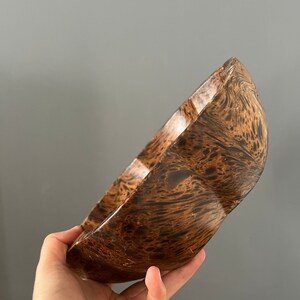 K&ouml;nnte beinhalten: Eine braune Holzschale mit einem einzigartigen Marmormuster. Die Schale ist leicht gekr&uuml;mmt und hat eine glatte, polierte Oberfl&auml;che.