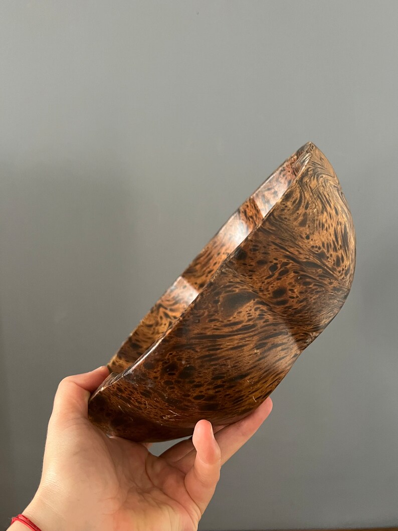 K&ouml;nnte beinhalten: Eine braune Holzschale mit einem einzigartigen Marmormuster. Die Schale ist leicht gekr&uuml;mmt und hat eine glatte, polierte Oberfl&auml;che.