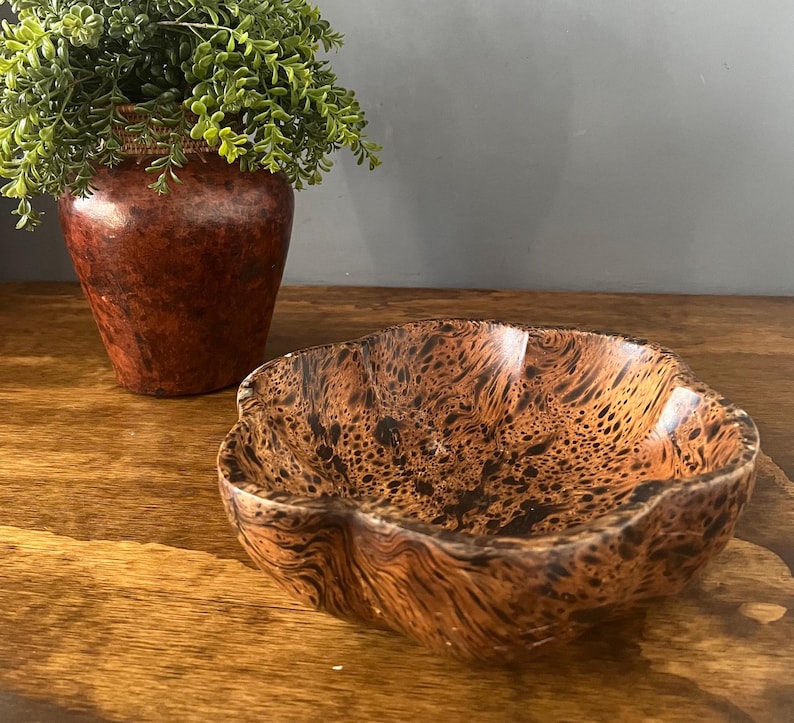 K&ouml;nnte beinhalten: Eine braune Holzschale mit einem einzigartigen Marmormuster. Die Schale hat eine wellige, organische Form und ist perfekt zum Servieren von Snacks oder Dekorationsartikeln.