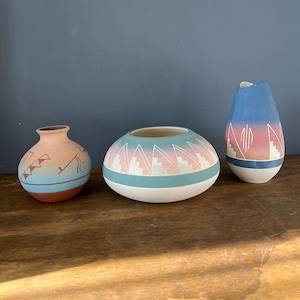 May include: Three ceramic vases with Southwestern-inspired designs. The largest vase is teal with pink and white geometric patterns. The medium vase is brown with blue and white geometric patterns. The smallest vase is blue with pink and white geometric patterns.