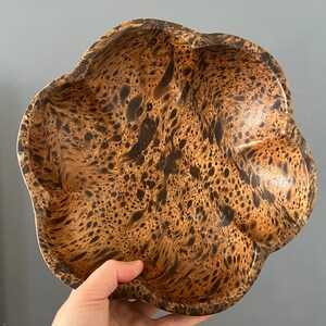 K&ouml;nnte beinhalten: Eine braune Holzschale mit einem einzigartigen Marmormuster. Die Schale hat eine wellige, unregelm&auml;&szlig;ige Form und eine glatte, polierte Oberfl&auml;che.