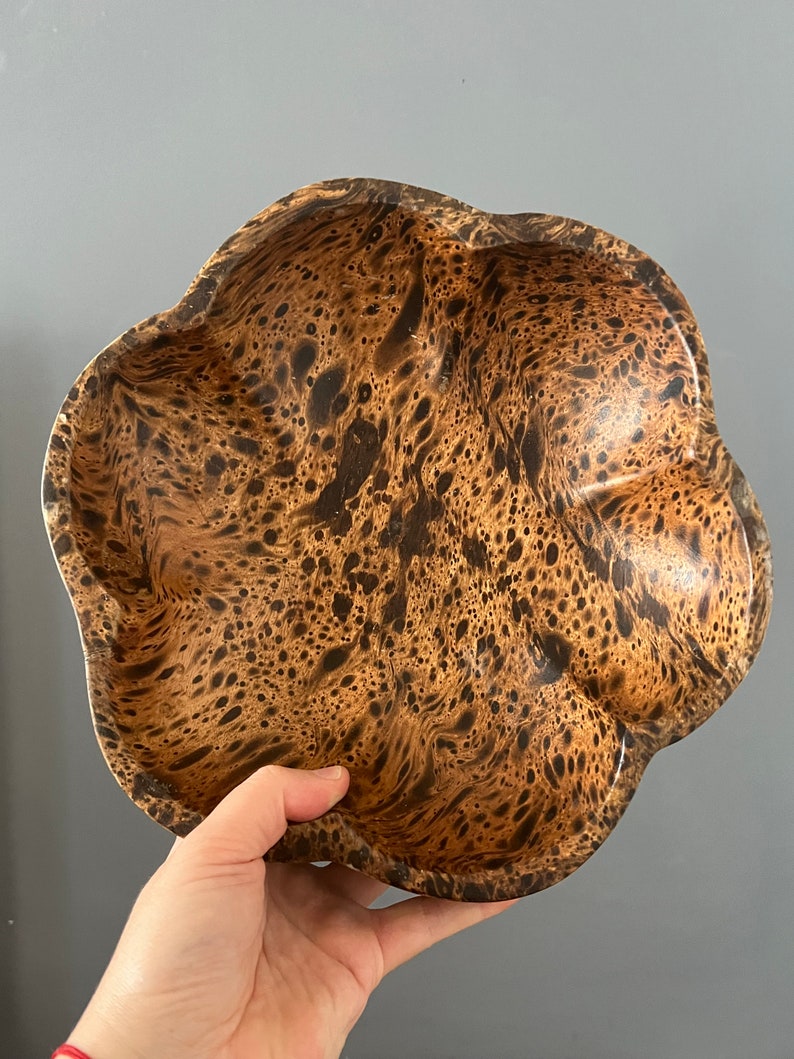 K&ouml;nnte beinhalten: Eine braune Holzschale mit einem einzigartigen Marmormuster. Die Schale hat eine wellige, unregelm&auml;&szlig;ige Form und eine glatte, polierte Oberfl&auml;che.