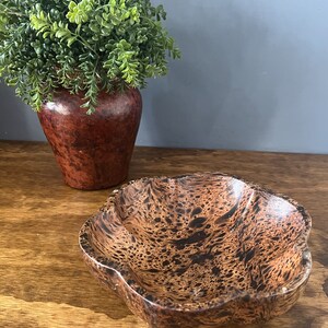 K&ouml;nnte beinhalten: Eine braune Holzschale mit einem einzigartigen Marmormuster. Die Schale hat einen abgerundeten, gewellten Rand und ist perfekt zum Servieren von Snacks oder zum Aufbewahren von kleinen Gegenst&auml;nden.