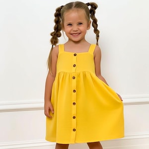 Könnte beinhalten: Ein leuchtend gelbes Kleid mit Knopfleiste und quadratischem Ausschnitt. Das Kleid wird mit braunen Sandalen getragen. Das Mädchen hat ihr Haar in zwei Zöpfen geflochten.