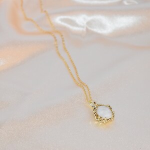 Op de afbeelding: Een gouden ketting met een witte ovale hanger in een gouden filigraan frame.