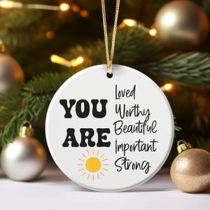 May include: White ceramic ornament with a yellow sun and the text "YOU ARE Loved Worthy Beautiful Important Strong".