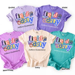 May include: Five colorful t-shirts in orchid, violet, neon violet, ivory, and seafoam. Each shirt features the words "field day" in a playful font, along with a whistle and clock graphic, and the text "Jeffers Elementary".