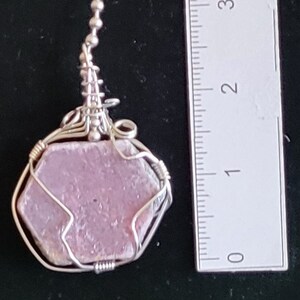 May include: A pink ruby gemstone pendant wrapped in silver wire. The pendant is approximately 1 inch in diameter.