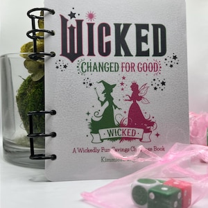 May include: A spiral-bound notebook with the word "WICKED" in large, stylized letters. The cover features illustrations of a witch and a fairy, with the text "CHANGED FOR GOOD" and "A Wickedly Fun Savings Challenge Book."