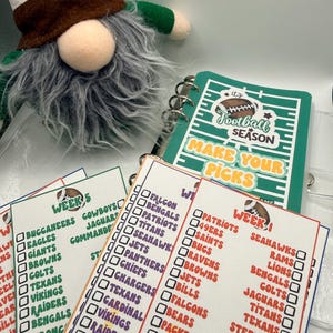 May include: A football-themed spiral-bound planner with a green field cover reading "It's Football Season Make Your Picks" and several loose-leaf tracking sheets featuring team names, checkboxes, and "Week" headers, accompanied by a plush gnome.
