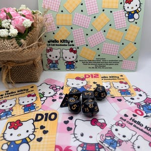 May include: A Hello Kitty themed game set featuring cards, dice, and a game board. The cards have a pink and yellow checkered pattern and feature the Hello Kitty character. The dice are black with gold numbers. A bouquet of pink roses is also present.