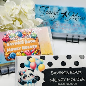 May include: Three money holder binders. One has a panda holding balloons, another says "Travel More", and the third has a seashell design. All have the words "Savings Book Money Holder" printed on them.