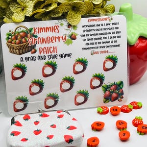 Peut inclure: Une pochette blanche à motif de fraises et une carte de jeu avec des fraises et le texte "Kimmie's Strawberry Patch A grab and save game". La carte de jeu contient des instructions pour un jeu où vous choisissez une fraise et enregistrez le montant indiqué au dos. Il y a aussi 10 petits jetons de fraises rouges et verts avec des numéros dessus.