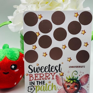 May include: A white card with brown circles and yellow stars. The card has the text "Sweetest Berry in the patch" with a cartoon strawberry with wings. The text below says "Total Saved $75+ Range: $1-$12 Save ___ for each yellow star!"
