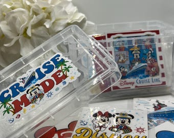 Op de afbeelding: Een transparante plastic opbergdoos met een Mickey Mouse en Minnie Mouse Disney Cruise Line sticker aan de voorkant. De doos is gevuld met kleine, transparante plastic zakjes met verschillende Disney Cruise Line stickers. De stickers bevatten Mickey Mouse, Minnie Mouse, Donald Duck, Goofy en andere Disney-figuren.