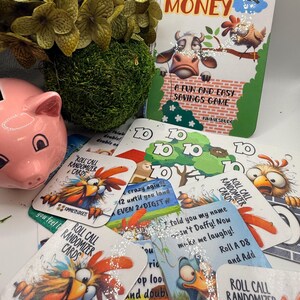 以下が含まれることがあります： ピンク色の豚の貯金箱が、「Funny Money」カードと「Roll Call Randomizer Cards」のデッキの隣にあります。ゲームボックスには牛と鶏のイラストが描かれています。カードには、漫画のオンドリとアヒルのグラフィックとテキストがあります。