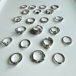 Puede incluir: Un conjunto de 18 anillos de plata con varios dise&ntilde;os, incluyendo mariposas, corazones y formas geom&eacute;tricas.