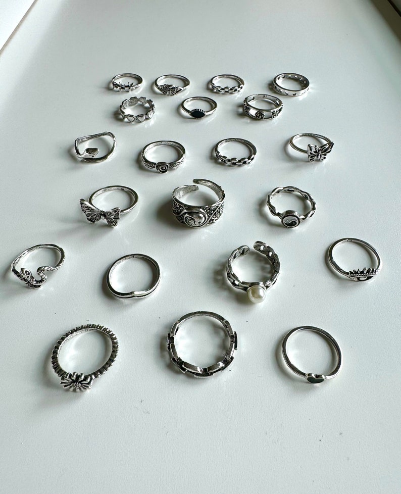 Puede incluir: Un conjunto de 18 anillos de plata con varios dise&ntilde;os, incluyendo mariposas, corazones y formas geom&eacute;tricas.