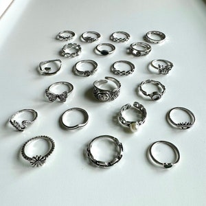 Puede incluir: Un conjunto de 18 anillos de plata con varios dise&ntilde;os, incluyendo mariposas, flores, corazones y patrones geom&eacute;tricos.