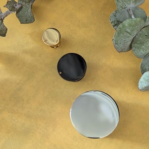 May include: Three round metal discs in different sizes. The smallest disc is gold, the middle disc is black, and the largest disc is silver.