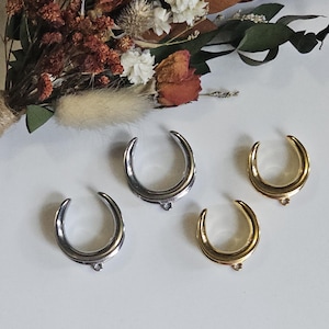 May include: Four crescent moon-shaped pendants arranged in a group. Two of the pendants have a polished silver-tone finish, and two of the pendants have a polished gold-tone finish. Each pendant features a small circular loop at the bottom centre.