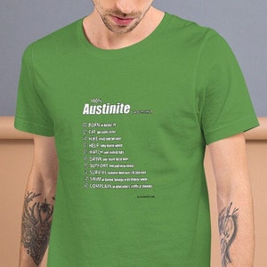 May include: A green t-shirt with a white graphic that says "Austin-ite" and lists a definition of the word. The definition includes words like "ride", "eat", "help", "watch", "give", "support", "laugh", "love", "listen", "create", "complete", and "inspire".