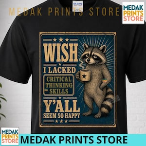 May include: A black t-shirt featuring a graphic of a raccoon holding a coffee mug. The text reads: WISH I LACKED CRITICAL THINKING SKILLS Y'ALL SEEM SO HAPPY. The design is framed in a rectangular border with star accents and radiating lines.