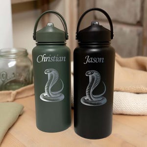 May include: Two insulated water bottles, one dark green and one black, with silver cobra designs. The green bottle has "Christian" and the black bottle has "Jason" printed on them. Both bottles have a black handle.