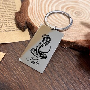Peut inclure: Porte-clés en argent avec un motif de cobra noir et le nom "Kyle" gravé dessus.
