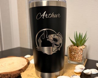 May include: A matte black stainless steel tumbler with a clear plastic lid. The front features a laser-engraved design of a person fishing with a large fish jumping out of the water, and the name Arthur is engraved in script above the graphic.