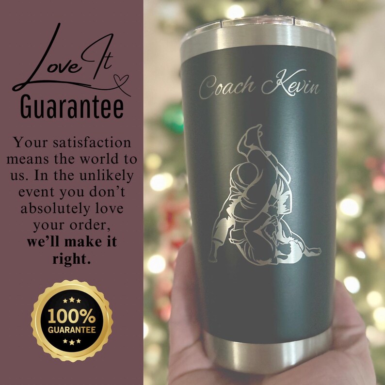 May include: A black and silver stainless steel tumbler with a personalized inscription that reads "Coach Kevin". The tumbler features a silver engraving of a person performing a grappling move.