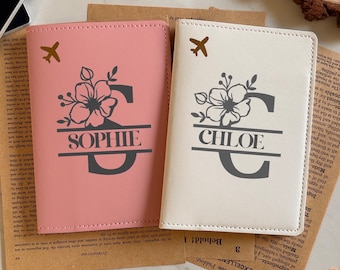 May include: Two personalized passport holders, one blush pink and one cream, are displayed. Each features a floral design with a letter and name: "Sophie" and "Chloe." A small airplane graphic is above the floral design. The passport covers are on a wooden surface.